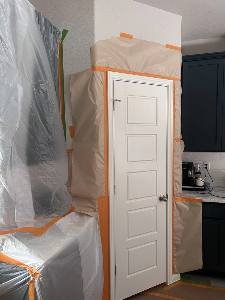 Kitchen doorway and cabinets masked in plastic before spraying
