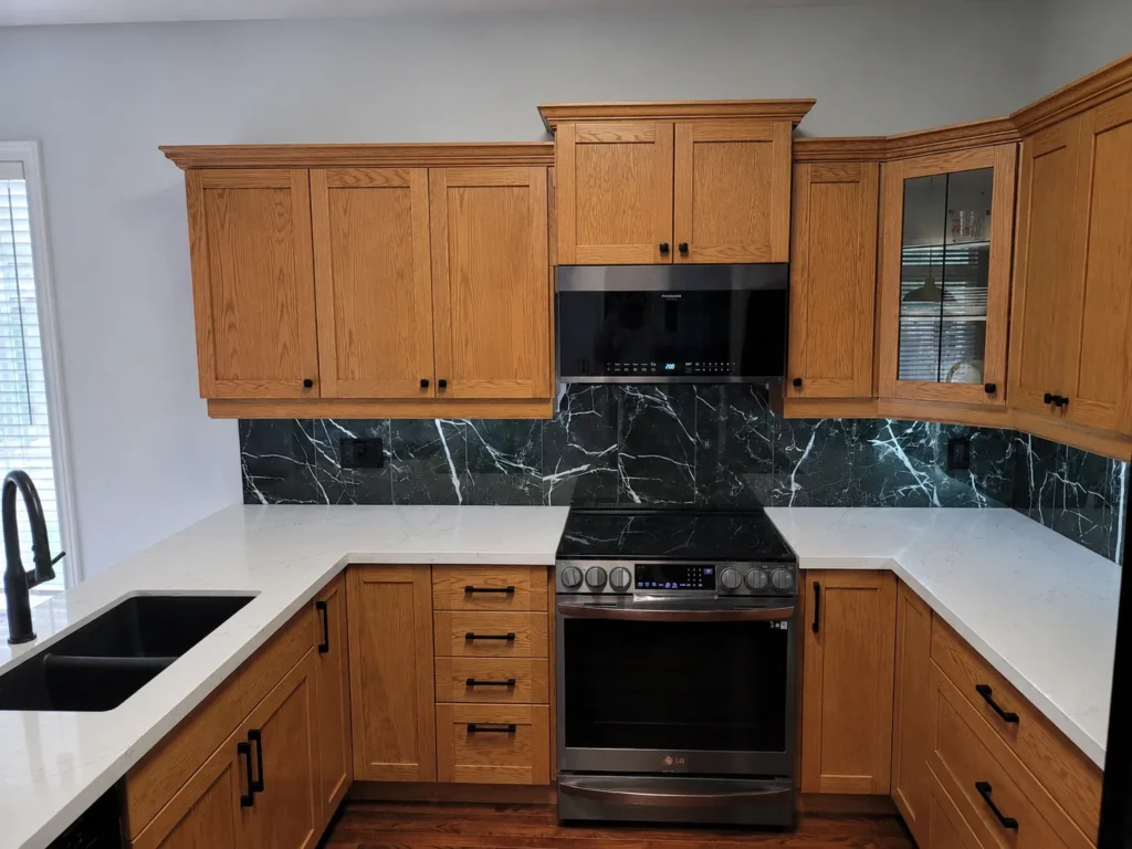 Kitchen with oak cabinets, dark marble backsplash and white countertops